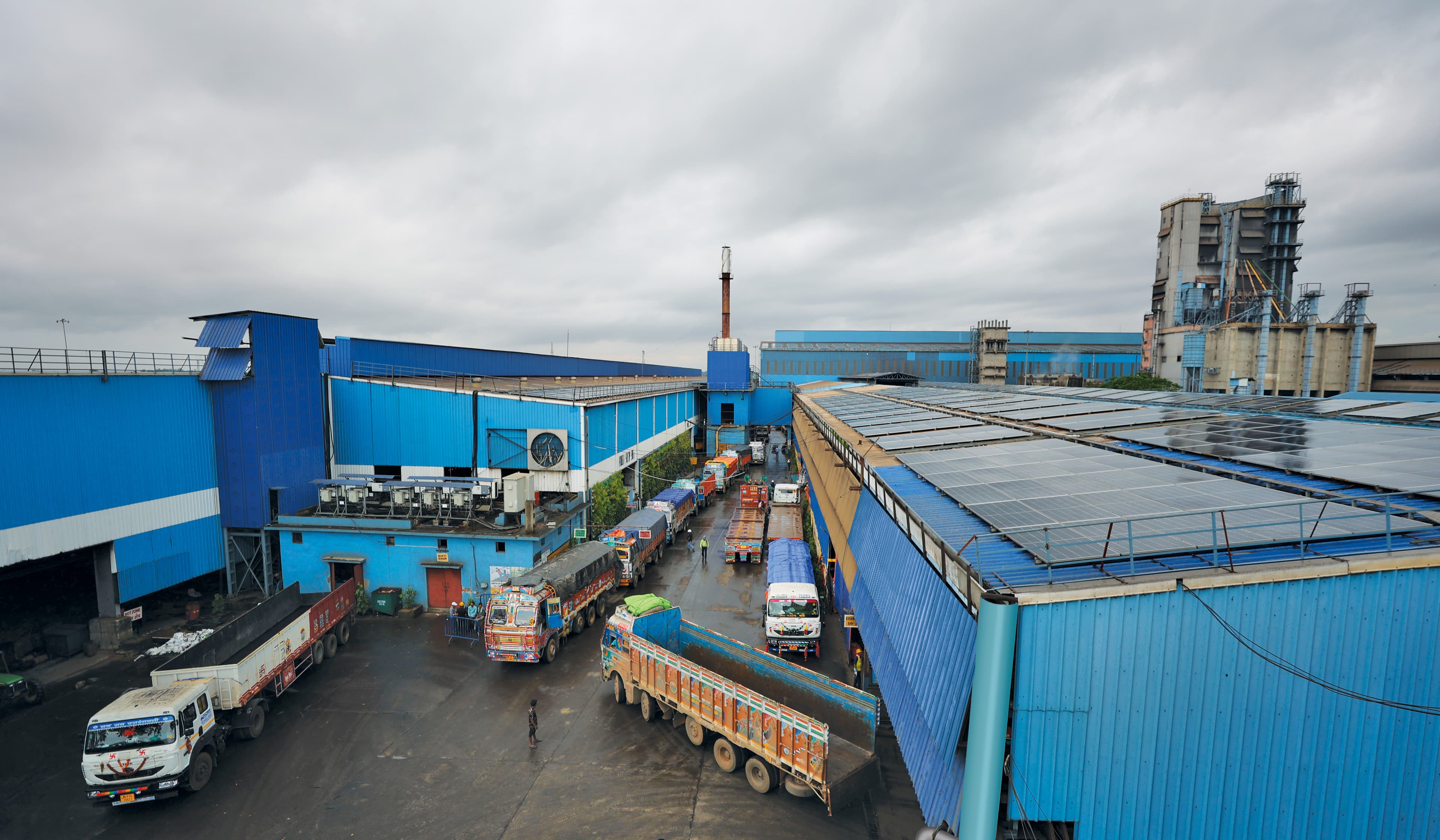 Aerial view of the SRMB plant — blue-clad production sheds with trucks loading in the yard